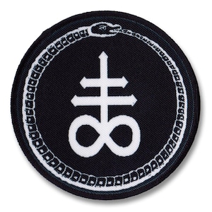 以下が含まれることがあります： 白と黒の刺繍パッチで、白い十字架のシンボルと下部に無限大のシンボルがあります。シンボルは、蛇のデザインが施された白い円に囲まれています。