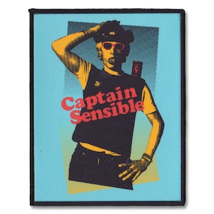 May include: A blue and yellow patch with a black outline featuring a cartoon image of a man wearing a yellow shirt, black vest, and a hat. The text "Captain Sensible" is printed in red and yellow letters.