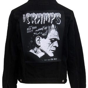 May include: Black denim jacket with a large white patch on the back featuring a band logo that says "The Cramps" and a black and white illustration of a monster. The text on the patch reads "Live in New York City!!" and "Friday 1 August The Ritz".