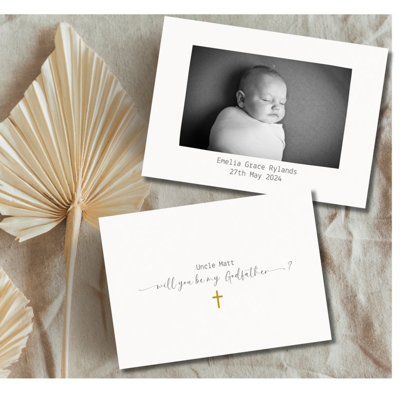 May include: A white card with a black and white photo of a baby. The text on the card reads "Emelia Grace Rylands 27th May 2024" and "Uncle Matt will you be my Godfather?" with a gold cross.