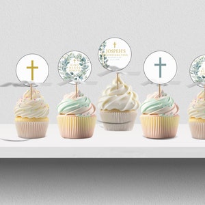 Op de afbeelding: Vijf cupcakes met decoratieve toppers. De toppers hebben een gouden kruis, een bloemenkrans met tekst en een blauwgroen kruis. De cupcakes hebben witte frosting en staan op een witte plank.