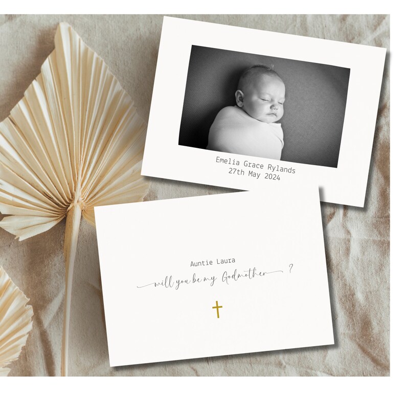 May include: A white card with black text asking "Auntie Laura, will you be my Godmother?" with a gold cross below. A black and white photo of a baby is on a separate card with the text "Emelia Grace Rylands, 27th May 2024."