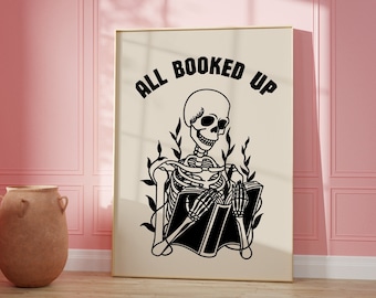 May include: A black and white illustration of a skeleton sitting and reading a book. The text "ALL BOOKED UP" is written in a circle around the skeleton.