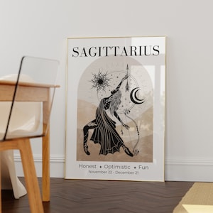 May include: A framed Sagittarius zodiac art print. The artwork features a black and white illustration of a woman with a bow and arrow, set against a beige and brown background with celestial elements. Text includes "SAGITTARIUS" and "Honest + Optimistic + Fun".