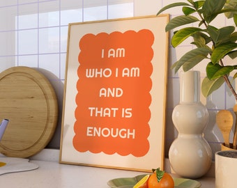 May include: A framed print with an orange background and white text that reads "I am who I am and that is enough". The print is sitting on a counter top in a kitchen setting.
