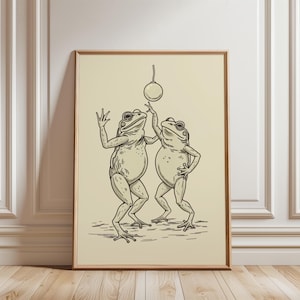 May include: A black and white line drawing of two frogs dancing. The frogs are wearing simple clothing and are holding a ball in the air. The drawing is on a cream background.