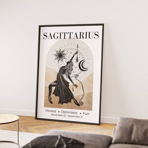 May include: A framed Sagittarius zodiac art print. The artwork features a black and beige illustration of a figure with a bow and arrow, with the word "SAGITTARIUS" at the top. The print also includes the words "Honest + Optimistic + Fun" and the dates November 22 - December 21.