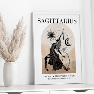 May include: A framed Sagittarius zodiac art print. The black and beige illustration features a woman with a bow and arrow, a sun, and a crescent moon. Text includes "Sagittarius", "Honest + Optimistic + Fun", and the dates November 22 - December 21.