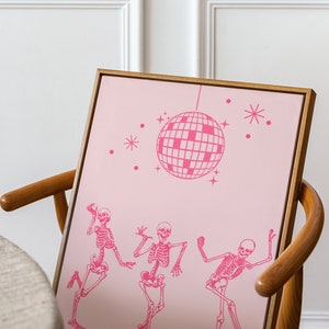 Puede incluir: Una impresi&oacute;n enmarcada en rosa y blanco con tres esqueletos bailando bajo una bola de discoteca. La impresi&oacute;n est&aacute; sobre un fondo rosa con estrellas blancas.