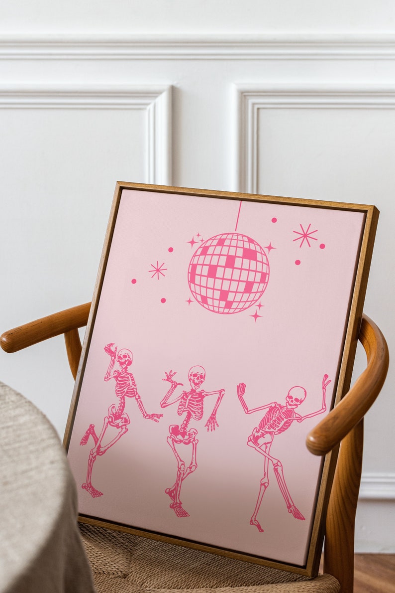 Puede incluir: Una impresi&oacute;n enmarcada en rosa y blanco con tres esqueletos bailando bajo una bola de discoteca. La impresi&oacute;n est&aacute; sobre un fondo rosa con estrellas blancas.