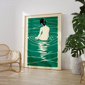 May include: A green and white abstract print of a woman sitting in a pool of water. The woman is facing away from the viewer and has dark hair. The print is framed in a light wood frame.