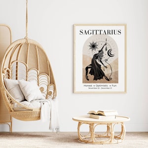 May include: A framed Sagittarius zodiac art print in a light wood frame. The black and beige artwork features a Sagittarius figure with a bow and arrow, with the words "Honest + Optimistic + Fun" below. A hanging wicker chair and a round table are also in the image.