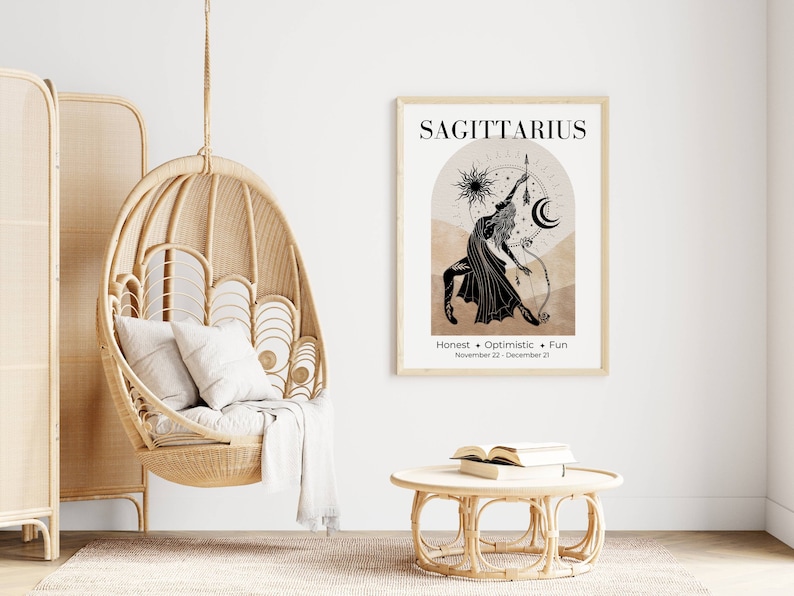 May include: A framed Sagittarius zodiac art print in a light wood frame. The black and beige artwork features a Sagittarius figure with a bow and arrow, with the words "Honest + Optimistic + Fun" below. A hanging wicker chair and a round table are also in the image.