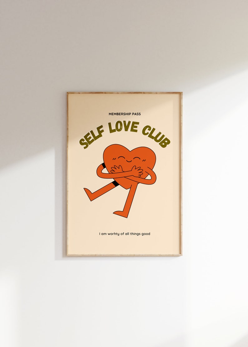 May include: A beige poster with a brown frame features a cartoon heart hugging itself. The text "SELF LOVE CLUB" is in green letters above the heart. The text "MEMBERSHIP PASS" is in smaller green letters above the text "SELF LOVE CLUB". The text "I am worthy of all things good" is in black letters below the heart.