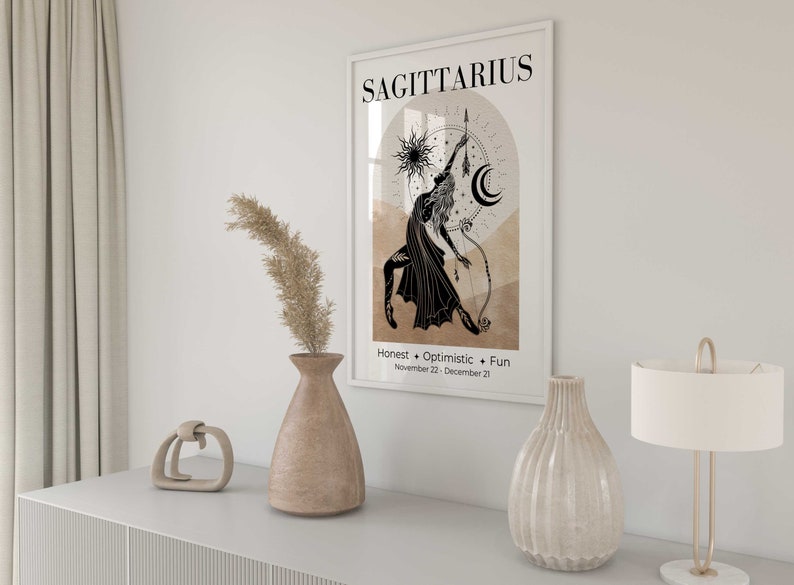 May include: A framed Sagittarius zodiac art print. The black and white illustration depicts a figure with a bow and arrow, set against a beige and brown background. The print includes the word "Sagittarius" and the traits "Honest, Optimistic, Fun."