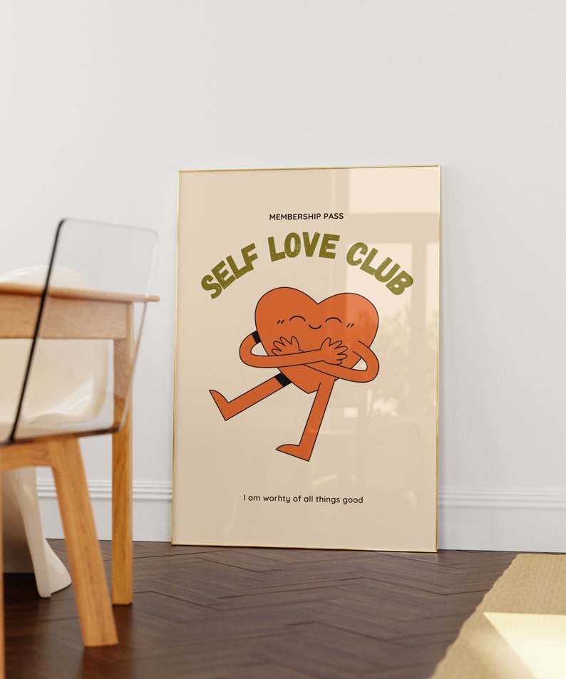 May include: A beige poster with a gold frame features a cartoon heart character with arms and legs hugging itself. The text "MEMBERSHIP PASS SELF LOVE CLUB" is in green letters above the heart. The text "I am worthy of all things good" is below the heart.