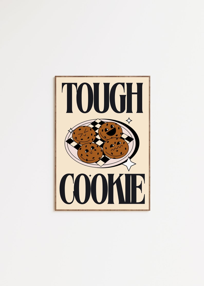 May include: A beige poster with a brown wooden frame. The poster features the text "TOUGH COOKIE" in black bold letters. There are four brown cookies with faces on a pink plate with a black and white checkered pattern.