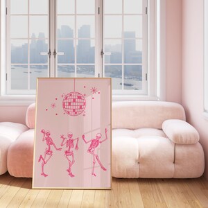 Puede incluir: Impresi&oacute;n art&iacute;stica enmarcada en rosa con una bola de discoteca rosa y tres esqueletos rosas bailando. La impresi&oacute;n est&aacute; colgada en una pared rosa en una habitaci&oacute;n con un sof&aacute; rosa.