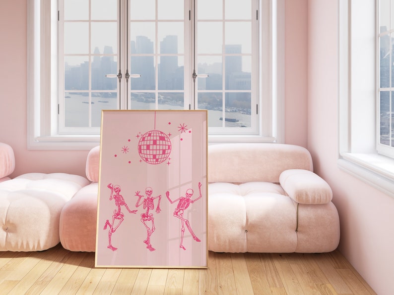 Puede incluir: Impresi&oacute;n art&iacute;stica enmarcada en rosa con una bola de discoteca rosa y tres esqueletos rosas bailando. La impresi&oacute;n est&aacute; colgada en una pared rosa en una habitaci&oacute;n con un sof&aacute; rosa.