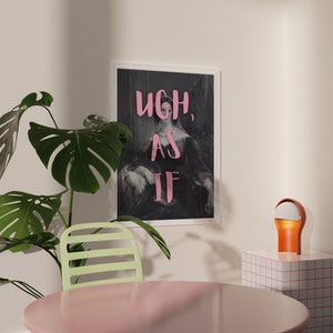 Puede incluir: Una impresi&oacute;n enmarcada en blanco y negro con el texto "Ugh, as if" en letras rosas. La impresi&oacute;n presenta a una mujer con un vestido y est&aacute; colgada en una pared blanca. Una planta verde est&aacute; en primer plano, y una peque&ntilde;a l&aacute;mpara naranja est&aacute; sobre una superficie de azulejos blancos.