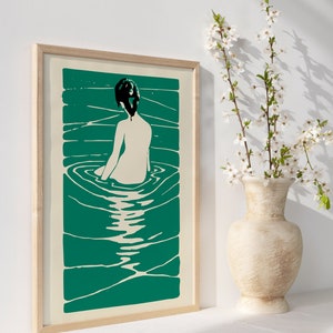 May include: A framed print of a woman sitting in a pool of water. The woman is depicted in a simple, minimalist style with a black silhouette and a white body. The water is a vibrant teal green color and is depicted with swirling lines.
