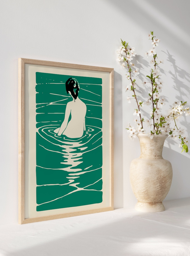 May include: A framed print of a woman sitting in a pool of water. The woman is depicted in a simple, minimalist style with a black silhouette and a white body. The water is a vibrant teal green color and is depicted with swirling lines.
