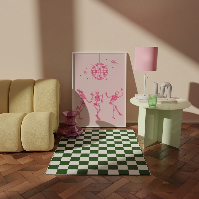 Puede incluir: Una alfombra a cuadros verdes y blancos delante de un sof&aacute; amarillo. Una l&aacute;mpara rosa con base blanca se encuentra sobre una mesa auxiliar verde claro. Un estampado enmarcado con una bola de discoteca rosa y esqueletos bailando cuelga de la pared.
