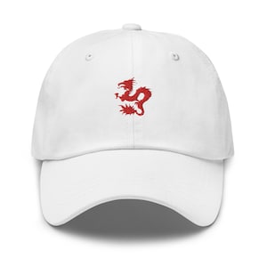 Pode incluir: Boné de beisebol branco com um design de dragão vermelho bordado na frente. O boné tem uma aba curva e uma alça ajustável na parte de trás. Um acessório clássico e casual.