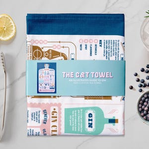 May include: A stack of three illustrated cotton tea towels with a blue band that reads "THE C&T TOWEL: AN ILLUSTRATED GUIDE TO GIN." The image includes lemon slices, a cocktail, juniper berries, and a pair of tongs.