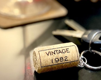 Op de afbeelding: Een bruine kurk sleutelhanger met de tekst "Vintage 1982" erop gegraveerd. De sleutelhanger heeft een zilveren metalen ring.