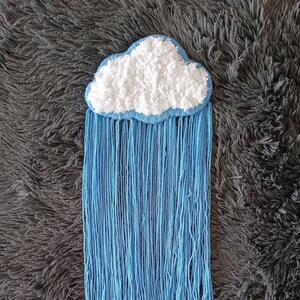 May include: A white fluffy cloud with blue yarn hanging down like rain. The cloud and yarn are attached to a gray fuzzy surface.