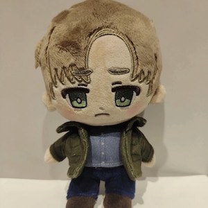 Op de afbeelding: Een pluche speelgoed van een cartoonfiguur met bruin haar, een groen jack, een blauwe spijkerbroek en bruine schoenen. Het personage heeft een droevige uitdrukking en groene ogen.