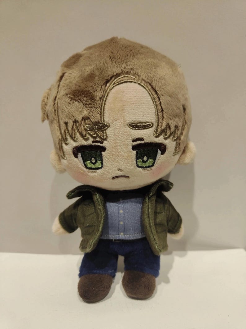 Op de afbeelding: Een pluche speelgoed van een cartoonfiguur met bruin haar, een groen jack, een blauwe spijkerbroek en bruine schoenen. Het personage heeft een droevige uitdrukking en groene ogen.