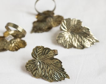 May include: Set of five gold leaf-shaped napkin rings. The rings are made of metal and have a detailed design.
