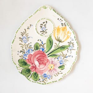May include: A teardrop-shaped ceramic serving plate with a cream-colored base and scalloped edges. The surface features hand-painted floral motifs including a large pink rose, a yellow tulip, and smaller blue flowers with green leaves.