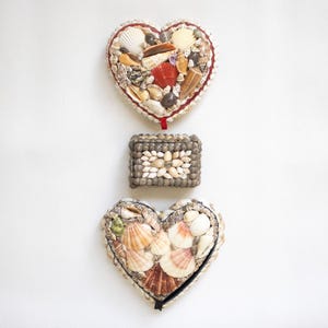 May include: Two heart-shaped boxes and one rectangular box covered in various seashells. The top heart box has a red ribbon, the middle rectangular box features a central flower pattern, and the bottom heart box is edged with a black ribbon.