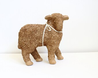 May include: A brown paper mache lamb figurine with a white ribbon tied around its neck.