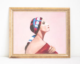 May include: A framed oil painting on a light pink background depicting a profile view of a figure wearing a red, white, and blue patterned headscarf and a red garment. The figure has dark hair, visible eyelashes, and is looking upward to the right.