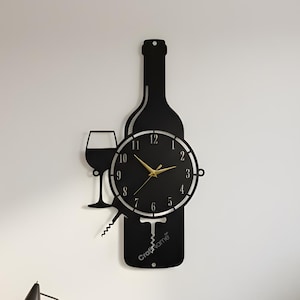 May include: Black metal wall clock in the shape of a wine bottle with a wine glass and corkscrew. The clock face is round with gold hands and numbers. The clock is mounted on a white wall in a living room setting.