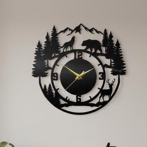 May include: Black metal wall clock featuring a forest scene with a wolf, bear, deer, and trees. The clock has gold-colored hands and a black face. The clock is mounted on a white wall in a living room setting.