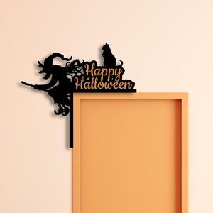 May include: Black metal Halloween decoration featuring a witch on a broom, a cat, and the words "Happy Halloween." The decoration is designed to be placed on a corner, with a door and a plant in the background.