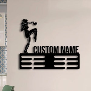 May include: Black metal medal display featuring a silhouette of a female boxer. The display has a space for a custom name and six rows of medal hooks.