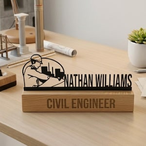 Puede incluir: Una placa de escritorio de madera con el nombre "NATHAN WILLIAMS" en negro, encima de las palabras "CIVIL ENGINEER". La placa presenta una silueta negra de un ingeniero civil en el trabajo. Un bolígrafo y una planta suculenta también están en el escritorio.