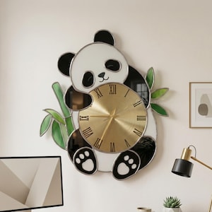 May include: A panda-shaped wall clock with a gold clock face and black Roman numerals. The clock features a white and black panda design with bamboo accents. The clock is mounted on a white wall above a wooden desk.