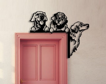 May include: Three black metal silhouettes of golden retriever dogs peeking over a pink door. The dogs are looking in different directions. The door has a gold handle and is closed. The background is a light beige wall with the text "CRAFTNAMESIGN" in black at the bottom.