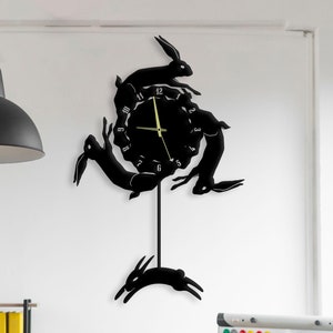 May include: Black wall clock with a silhouette of rabbits jumping around the clock face. The clock has a pendulum and is hanging on a white wall.