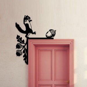 May include: Black metal squirrel and acorn door knocker with a leaf design. The knocker is mounted on a pink door.