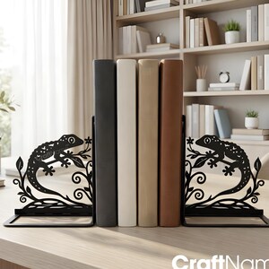 May include: Black metal bookends with a lizard design, holding up a row of books. The bookends feature a decorative lizard silhouette with floral accents. The books are in shades of black, white, beige, and brown. The CraftName sign is visible at the bottom.