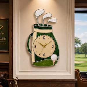 May include: A golf-themed wall clock shaped like a golf bag, featuring a cream-colored clock face with gold hands and black numerals. The bag is green and cream-colored, with three golf clubs and a golf ball. The clock is mounted on a beige wall.