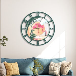 Könnte beinhalten: Eine grüne, metallgerahmte Uhr mit einem rosafarbenen Flamingo und Palmen im Rahmen. Die Uhr hat römische Ziffern und hängt an einer weißen Wand.